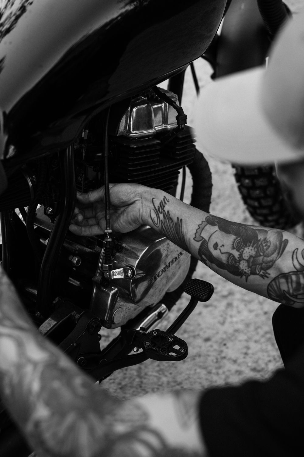 Black-and-white photograph of a hand working beside a motorcycle engine.